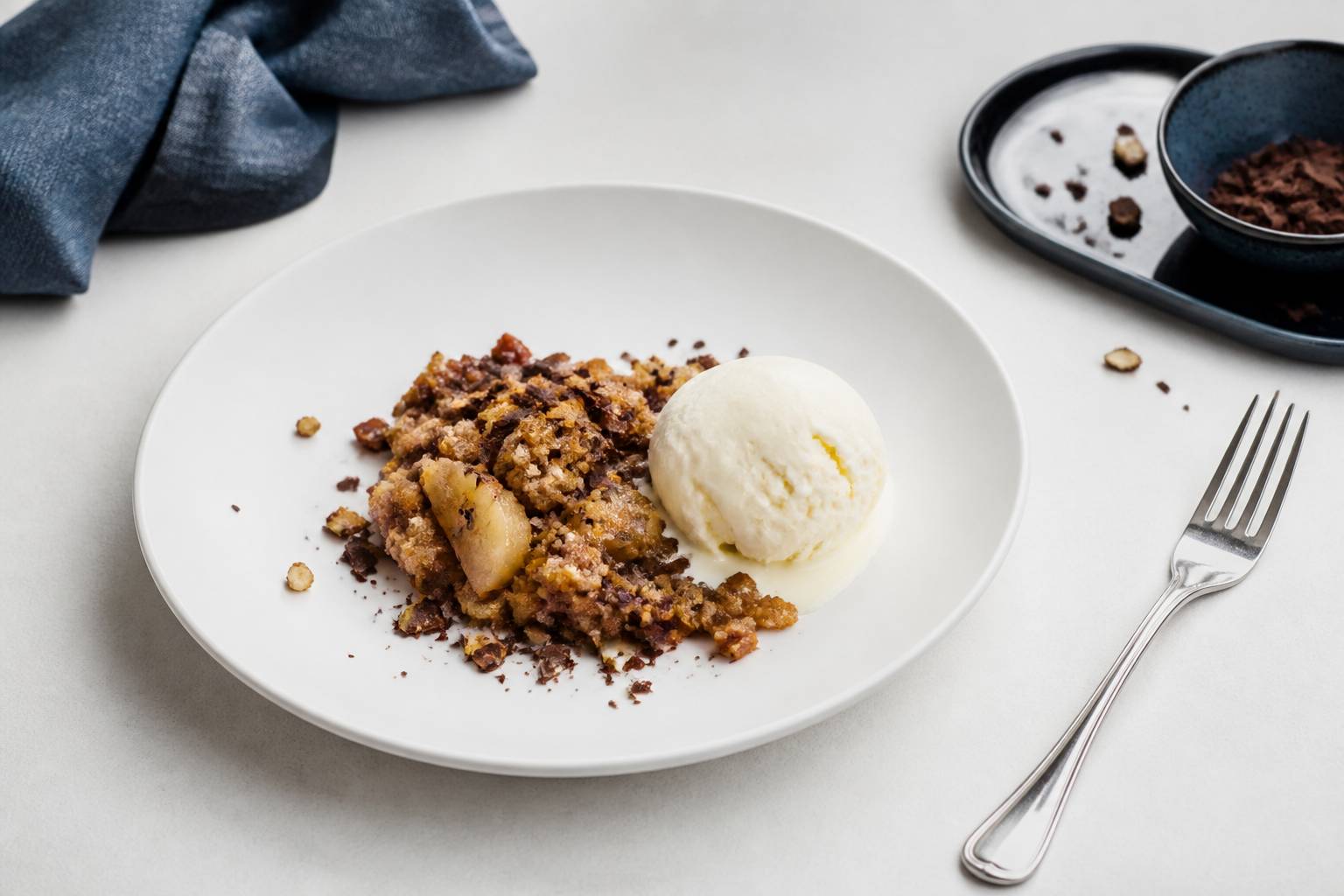 Crumble poires chocolat servi en assiette avec boule de glace vanille copeaux chocolat noisettes concassées