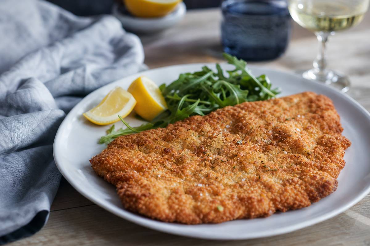 Escalope de veau milanaise servie avec quartiers de citron et roquette, verre de vin en arriegrave;re-plan